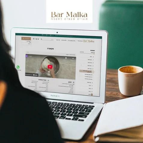 הדמיית מחשב נייד עם אתר Bar Malka, ליד ספל קפה על שולחן עץ.